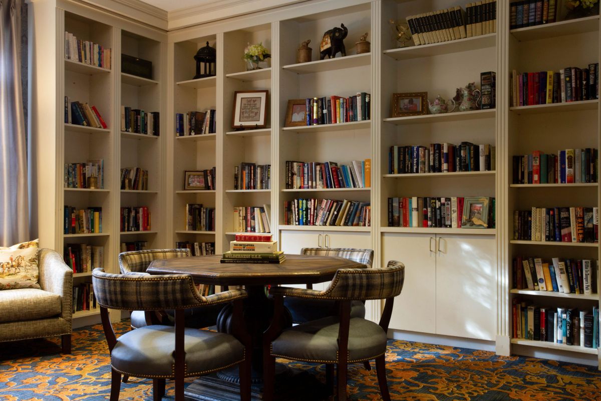 A cozy library with well-stocked bookshelves and a round table surrounded by chairs.