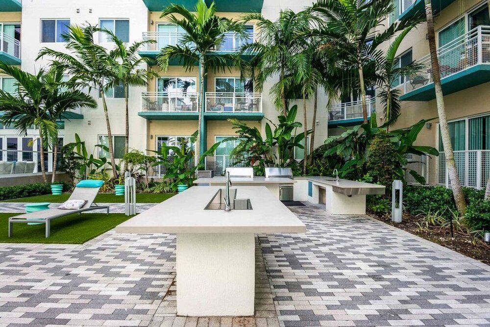A modern outdoor kitchen area surrounded by tropical greenery and apartment buildings.