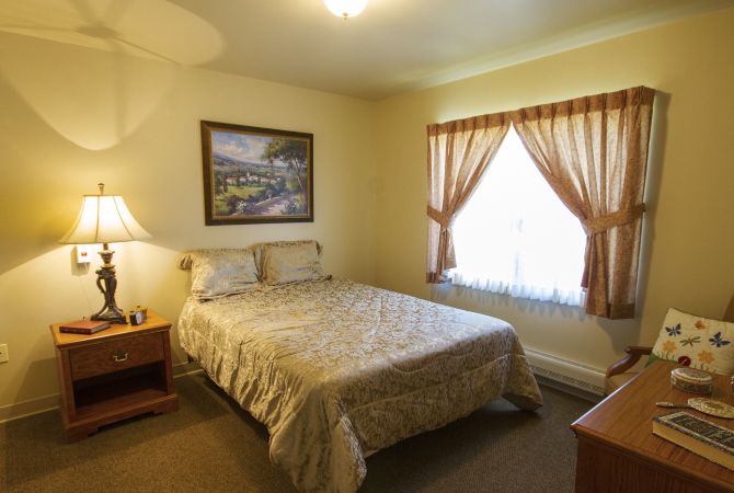 A cozy bedroom with a bed, nightstand, and a large window with curtains.