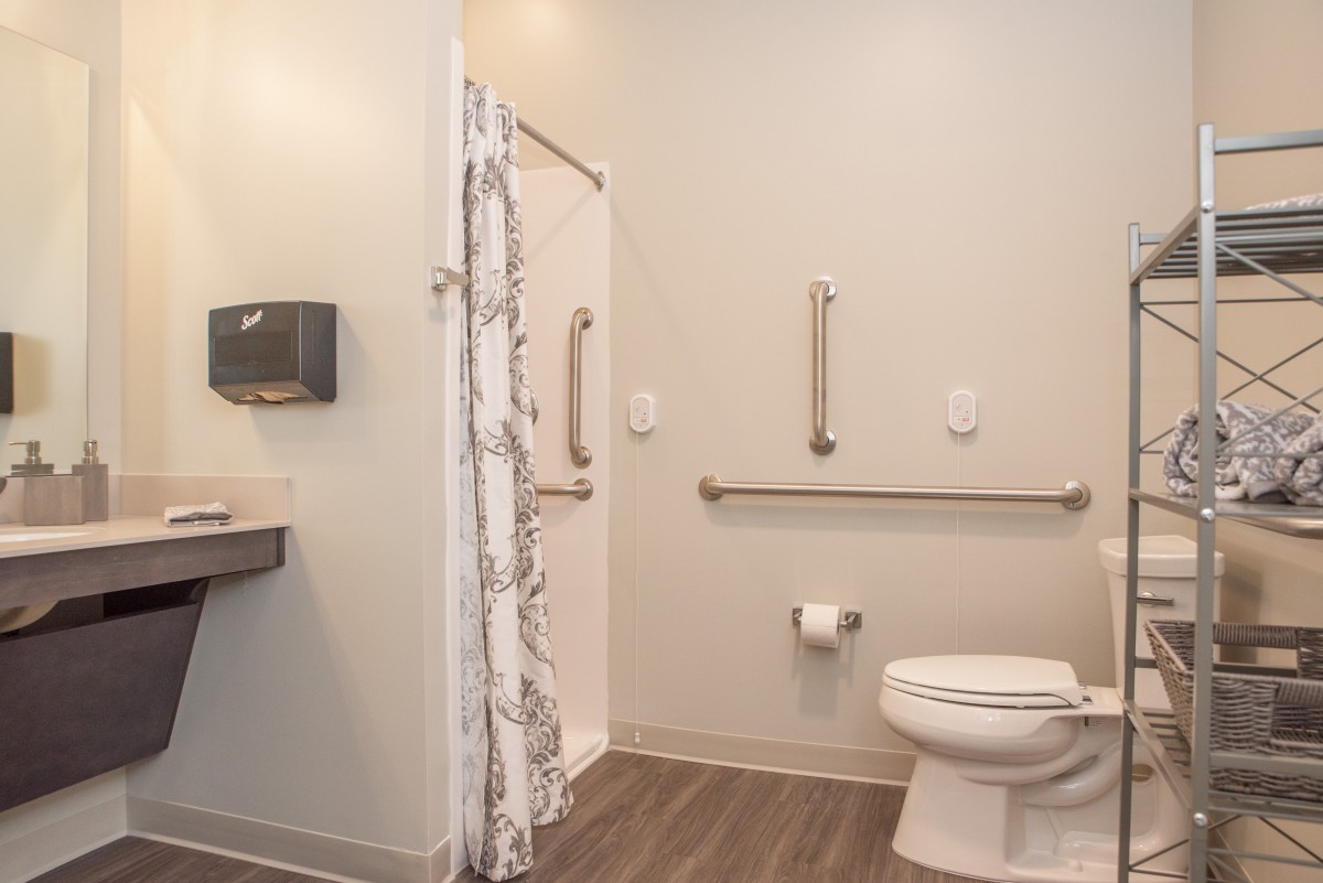 A modern, accessible bathroom featuring grab bars and a roll-in shower.