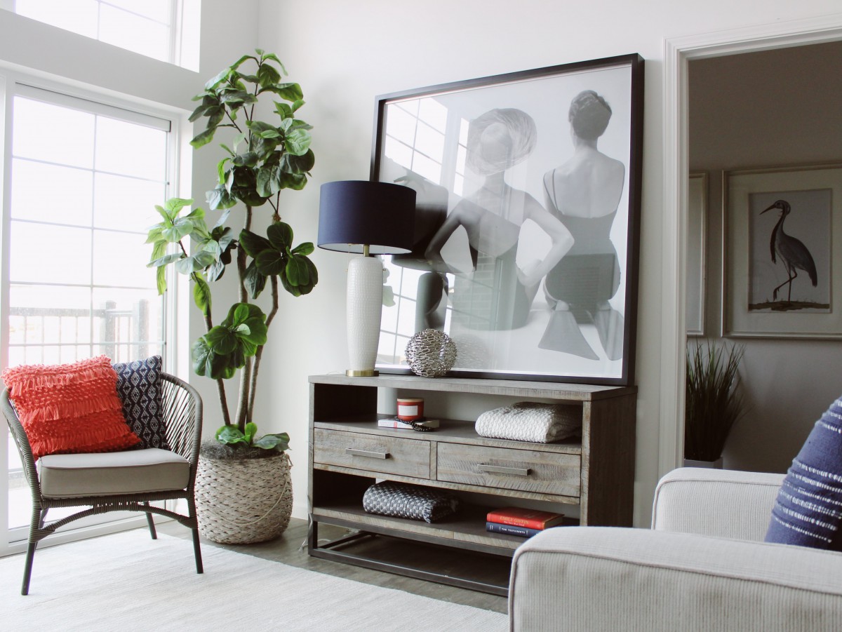 A stylish living room interior featuring a console table adorned with artwork, a lamp, and a large potted plant nearby.