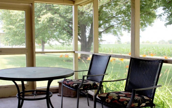 A serene screened porch with chairs and a table overlooking lush greenery.