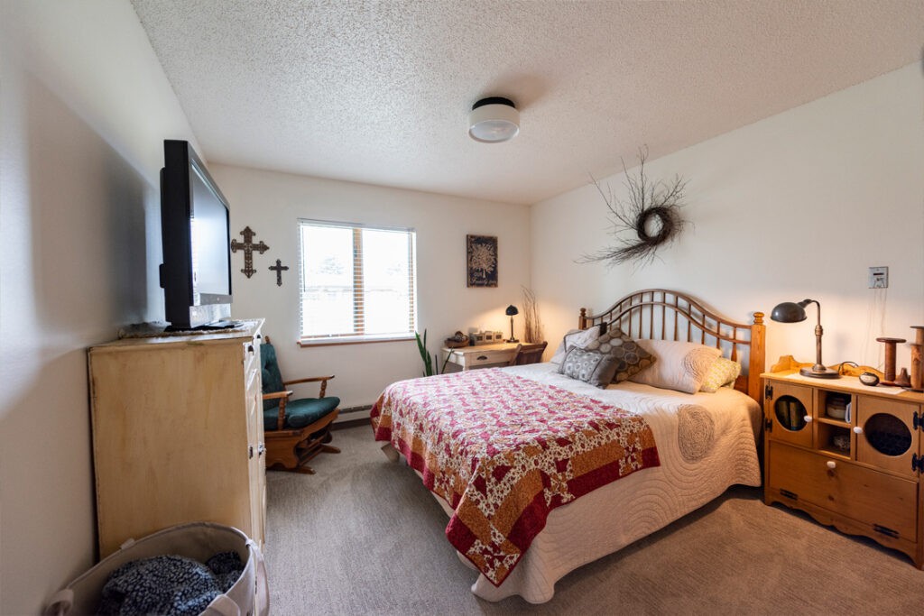 A cozy bedroom with a neatly made bed, television, and various decorative elements.