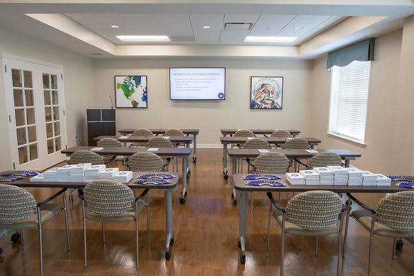 A well-organized conference room set up for a presentation with tables and chairs arranged in rows, facing a screen.