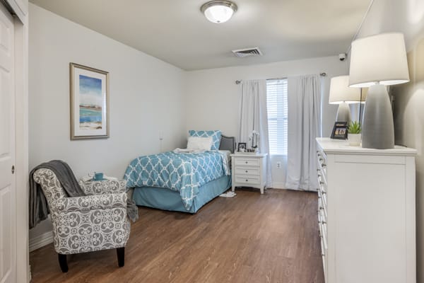 A cozy bedroom with a single bed, patterned chair, and hardwood flooring.
