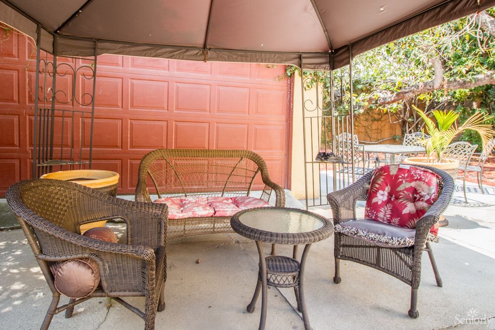 A cozy outdoor patio setup under a gazebo with wicker chairs, a swing bench, and a small round table.