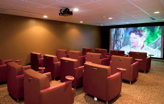 A cozy home theater setup with rows of comfortable chairs facing a large screen.