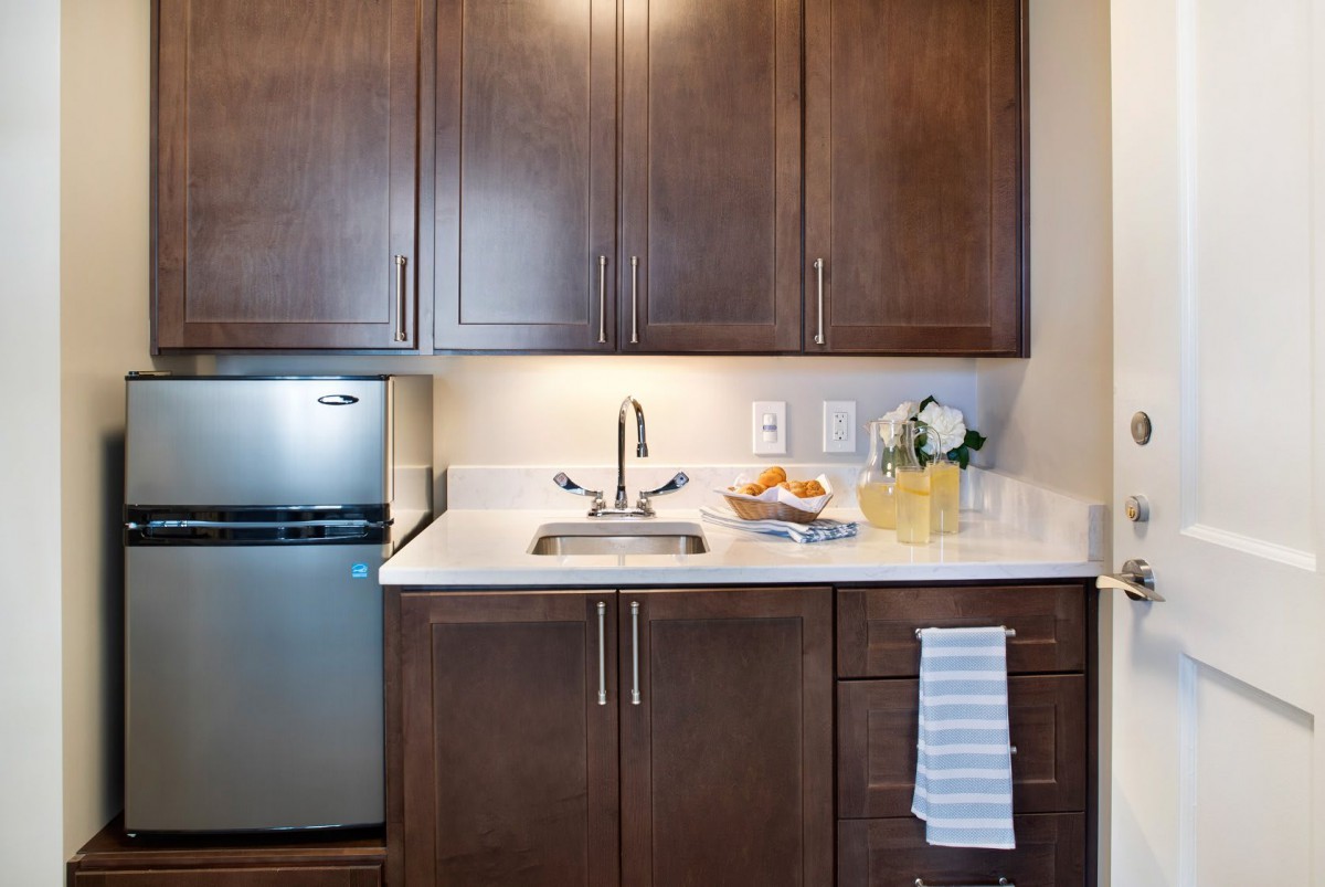 A compact kitchen area featuring dark wooden cabinets, a small fridge, and a clean countertop with a sink and decorative items.