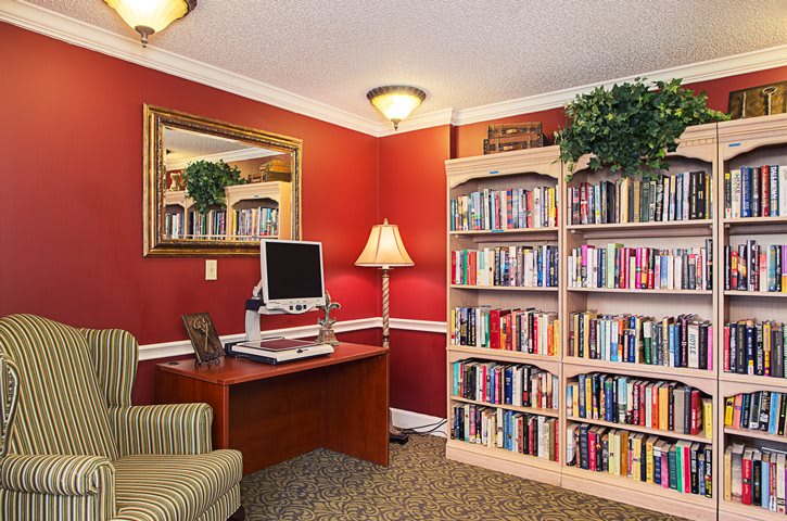 A cozy room with red walls featuring a bookshelf filled with books, a desk with a computer, an armchair, and a lamp, creating a warm and inviting reading space.