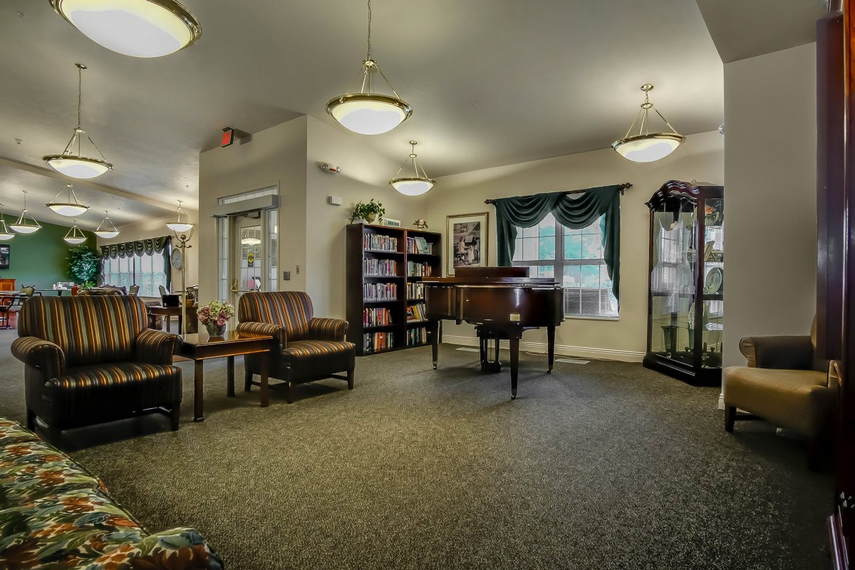 A cozy lobby area featuring comfortable seating, a piano, bookshelves, and large windows.