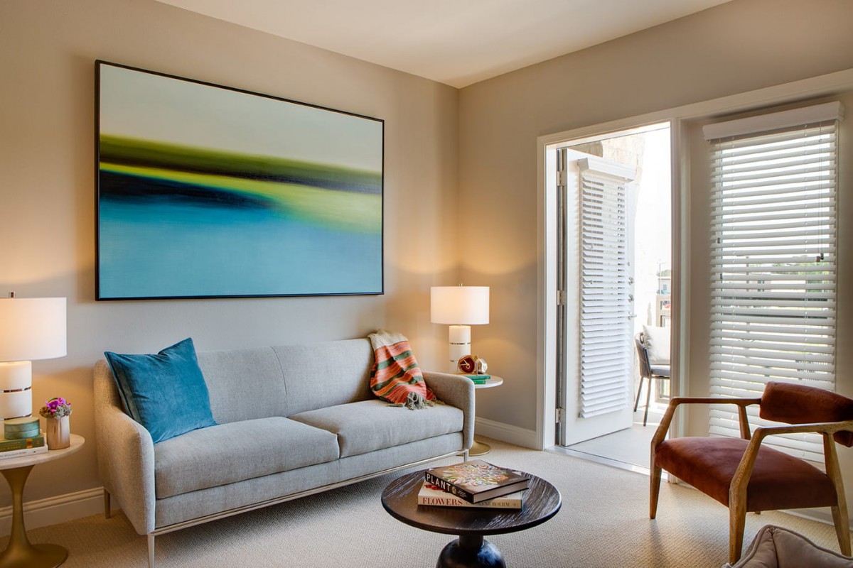 A cozy living room with modern decor featuring a sofa, colorful artwork, and a stylish lamp.