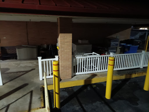 A dimly lit parking lot featuring a white fence and yellow safety poles near a building at night.