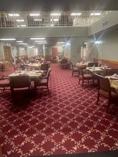 An empty dining room with neatly arranged tables and chairs on a patterned carpet.