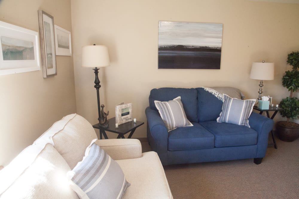 A cozy living room with a blue sofa and striped cushions, decorated with wall art and a lamp.