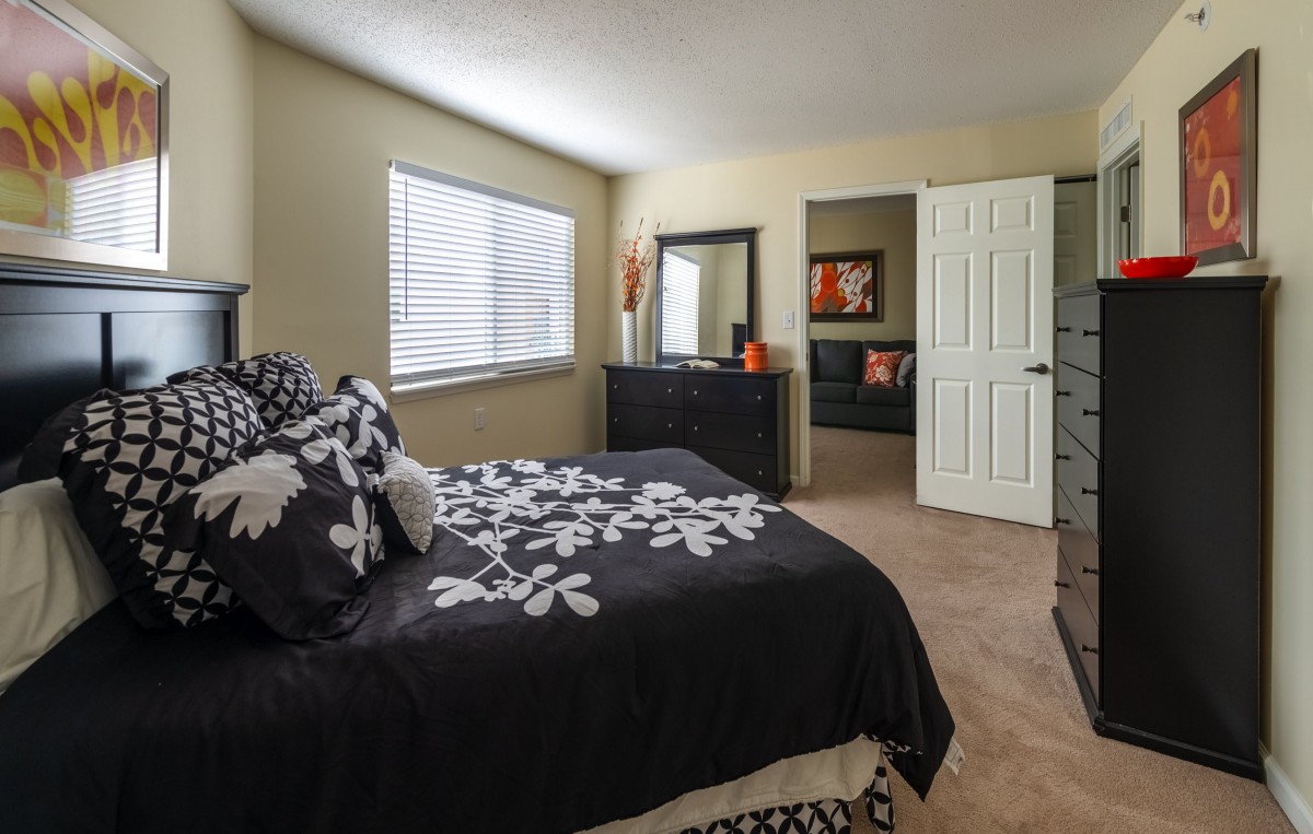A cozy bedroom with a neatly made bed, featuring black and white bedding and a mirror above a dresser near the window.