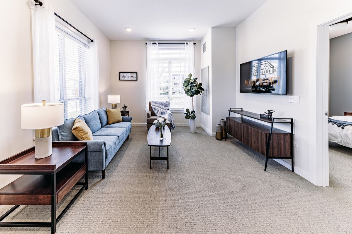A modern living room with a comfortable sofa, coffee table, and wall-mounted television, featuring bright lighting and stylish decor.