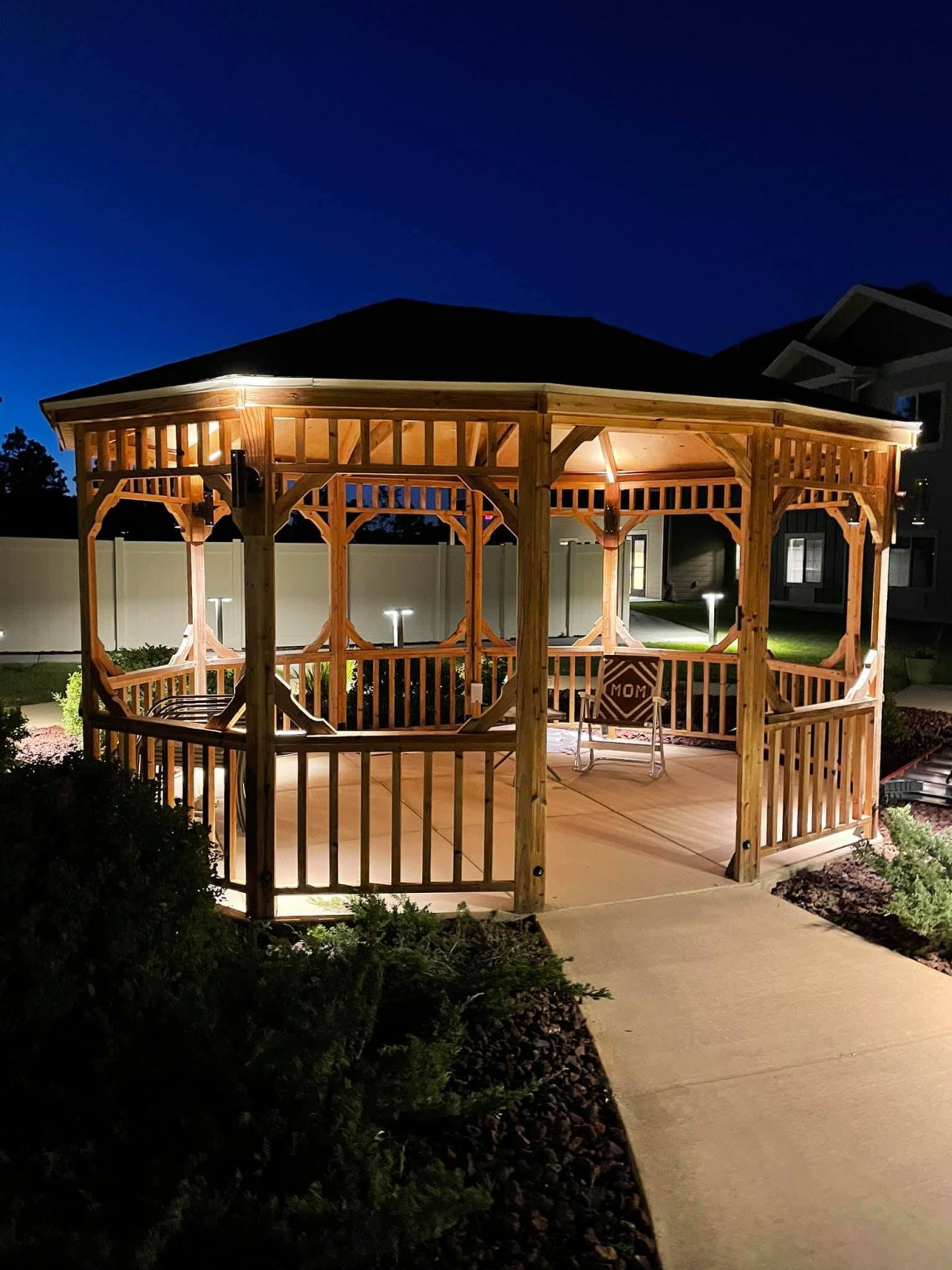 A beautifully lit wooden gazebo in a garden setting at night.