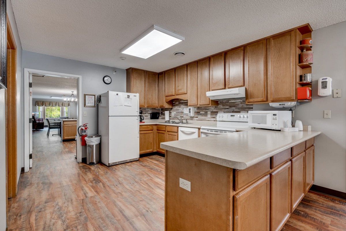 A spacious kitchen with wooden cabinets and white appliances, including a refrigerator and stovetop, featuring a hardwood floor.