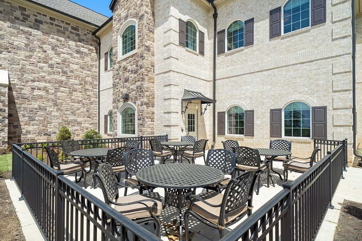 A spacious outdoor patio area with several tables and chairs, adjacent to a brick building with large windows.