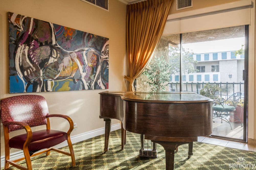 A sunlit room with a grand piano, artwork, and elegant furnishings.