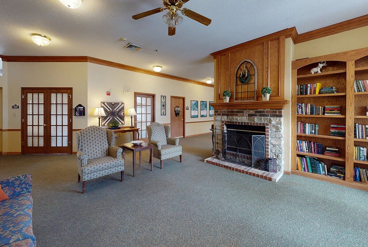 A cozy living room with a stone fireplace, two armchairs, and a ceiling fan.