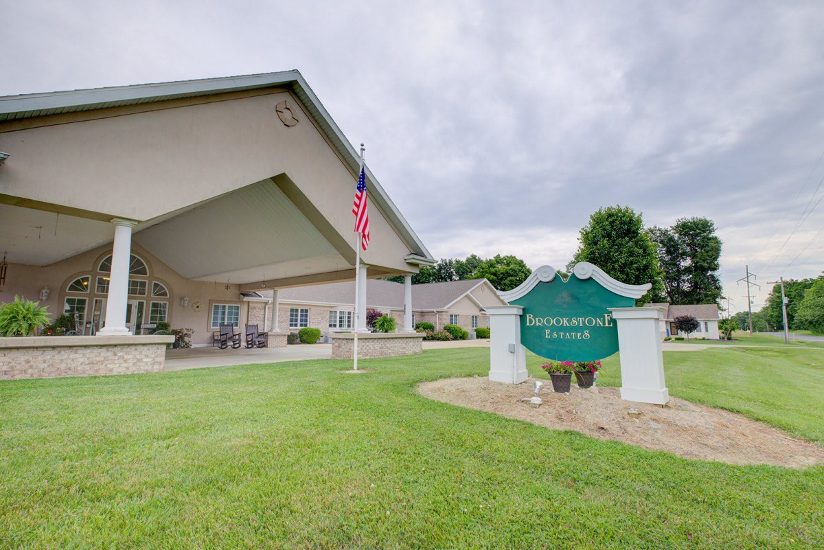 A building entrance with an American flag and a green sign on a well-maintained lawn under cloudy skies.