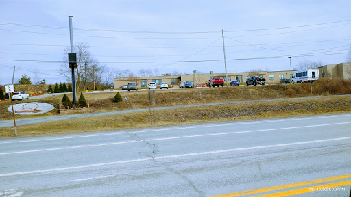 A view of a road lined with vehicles, leading to a building in the background under an overcast sky.