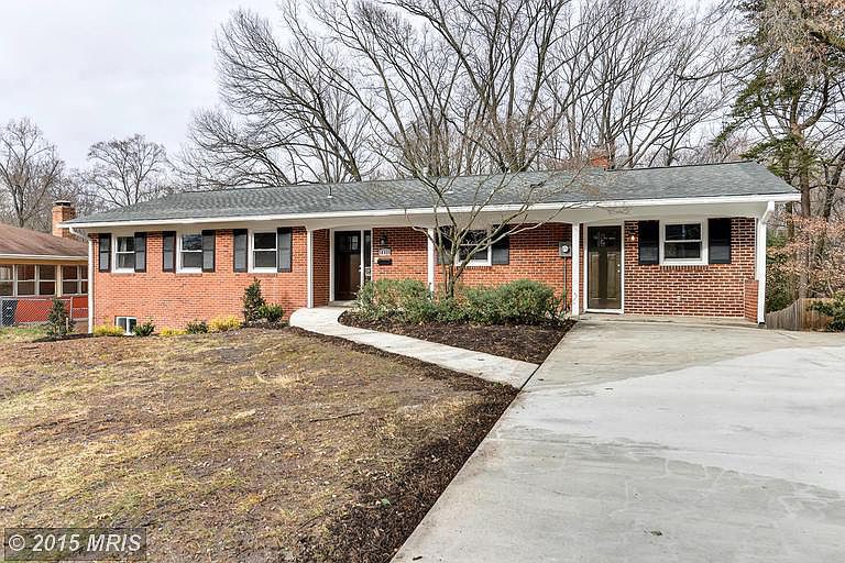 A brick ranch-style house with a driveway and bare trees in the background.