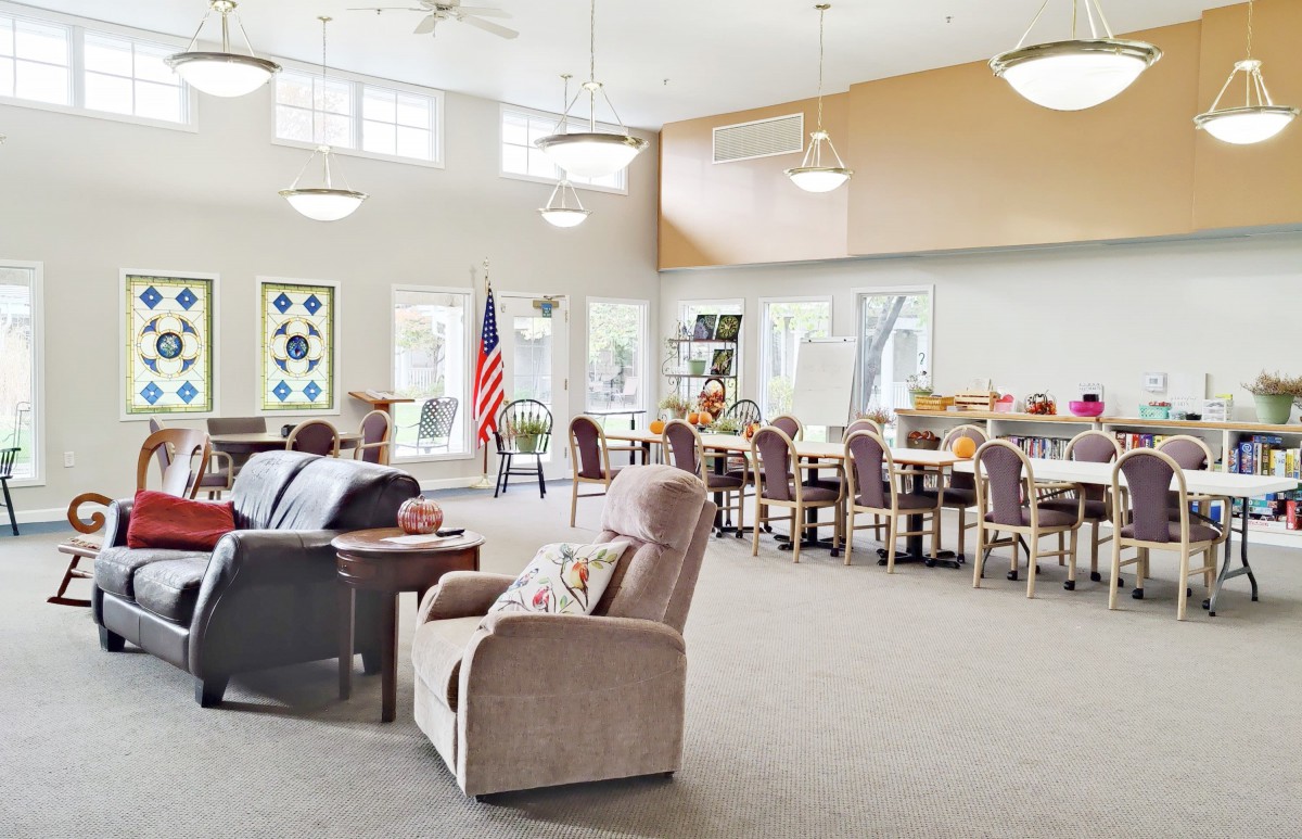 A spacious community center room furnished with tables, chairs, and an American flag on display.