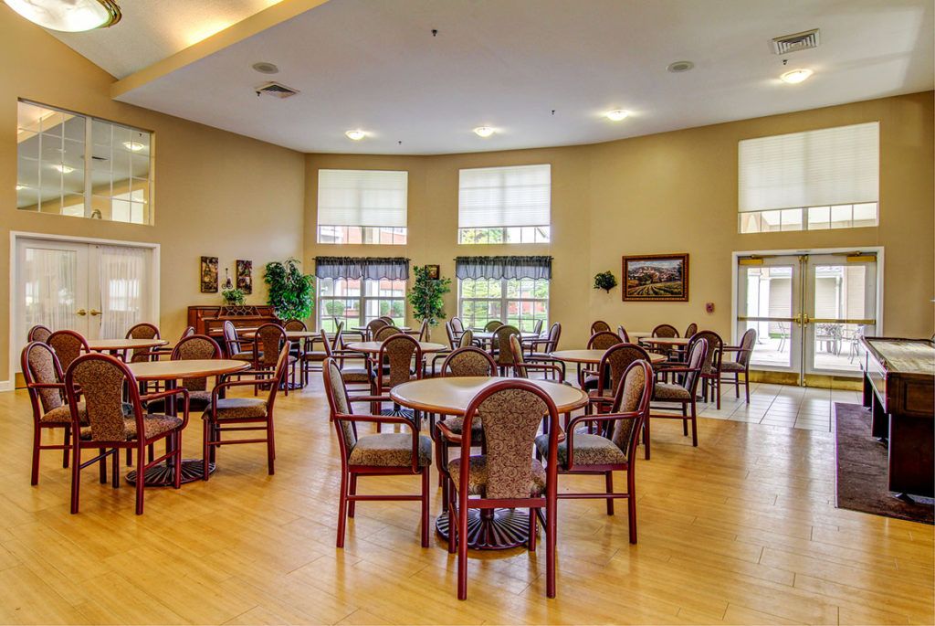A spacious dining area with multiple tables and chairs, large windows, and decorative plants.