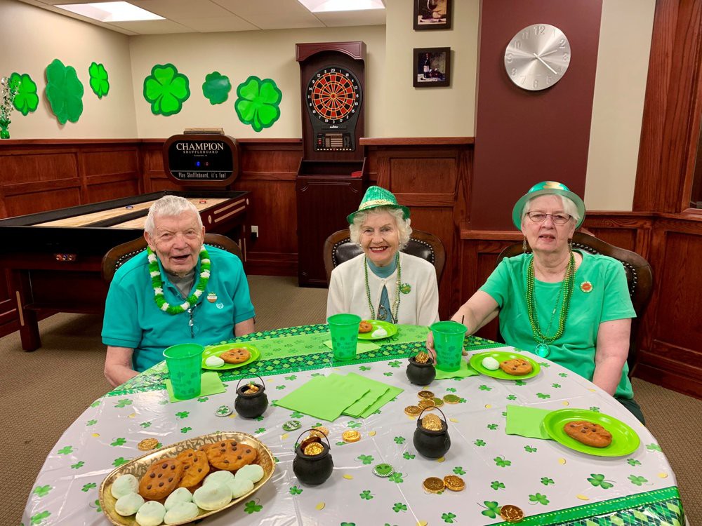 A joyful St. Patrick's Day celebration with three elderly friends dressed in green, surrounded by festive shamrock decorations and treats.