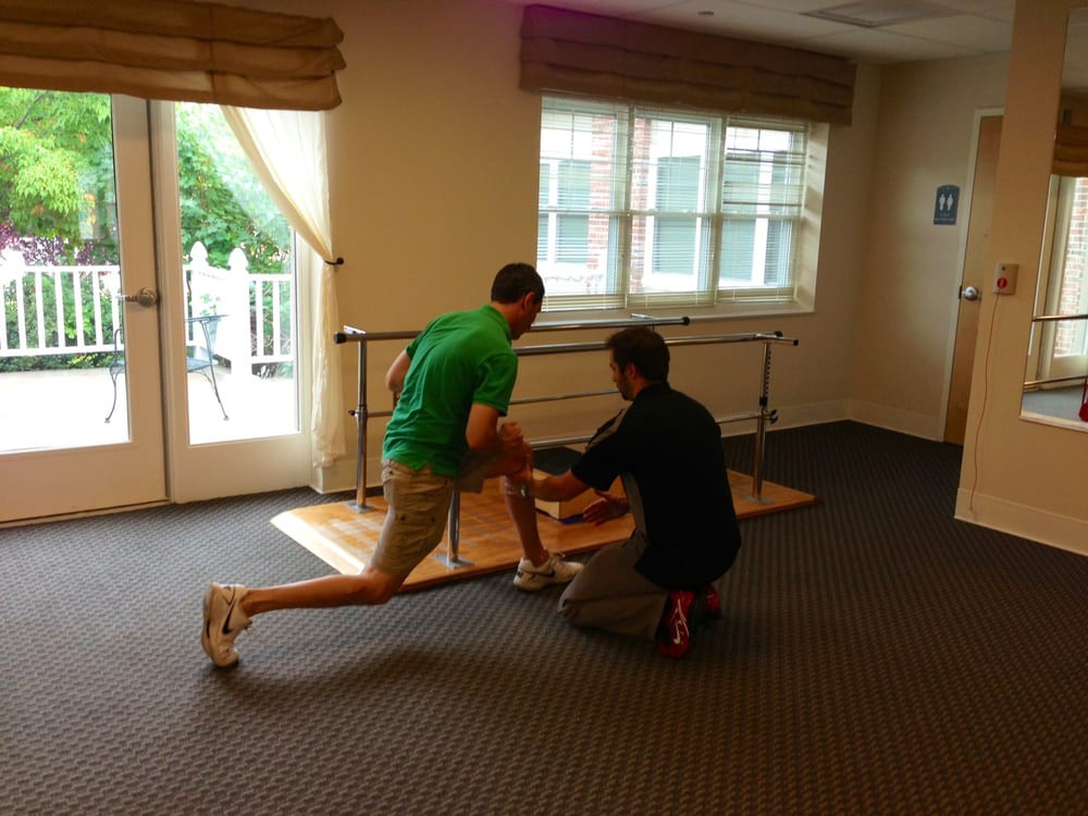 A physical therapy session with a person performing an exercise under the guidance of a therapist indoors.