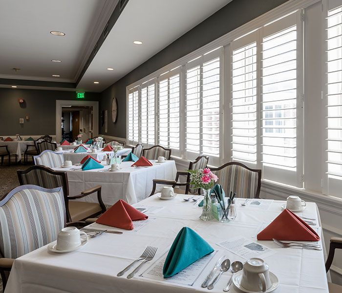A spacious dining room with neatly set tables and colorful napkins by large windows.