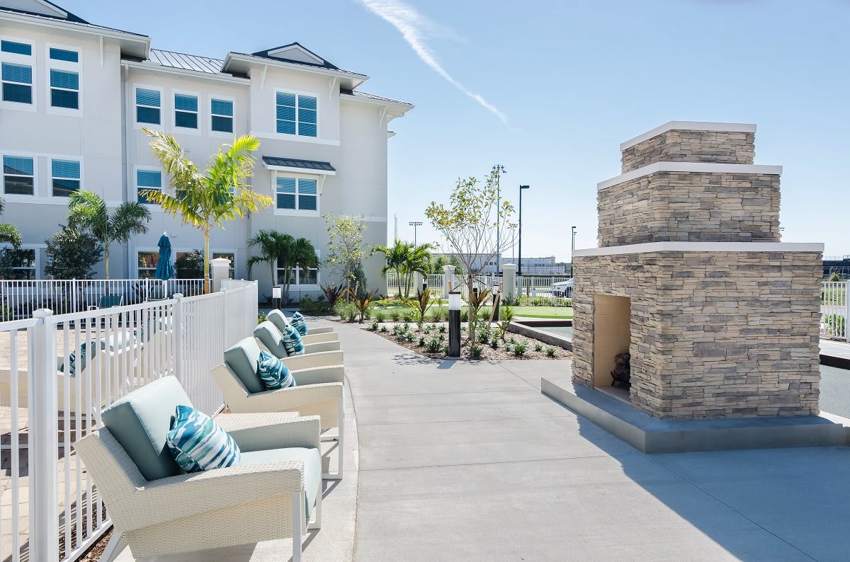 Outdoor seating area with chairs and a fireplace next to a modern building on a sunny day.