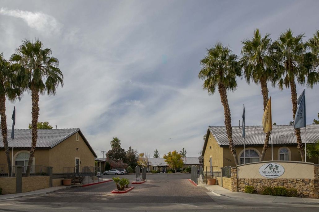 A suburban residential street with palm trees and houses under a cloudy sky.