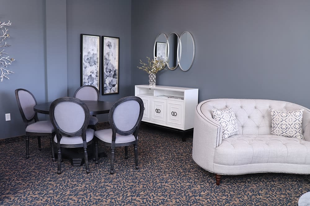 A stylish living room with a cozy white sofa, elegant dining chairs and table, complemented by wall mirrors and framed artwork.