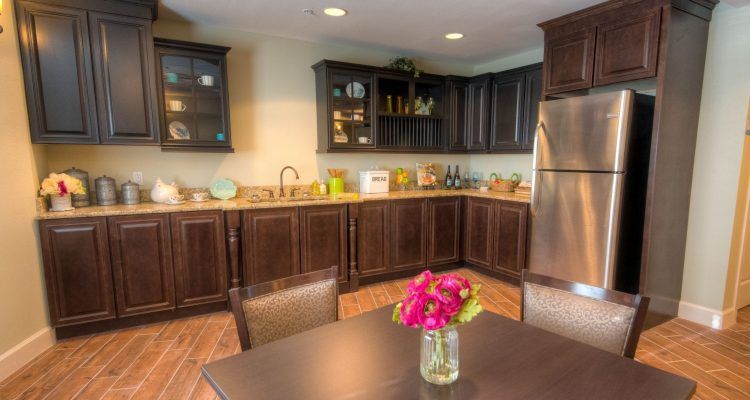 A modern kitchen with dark wooden cabinets and a stainless steel refrigerator, featuring a dining table with a vase of flowers.