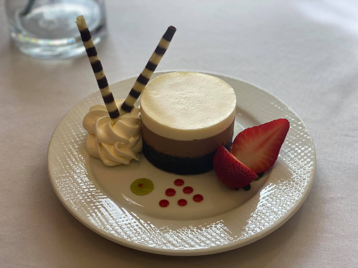 A beautifully presented layered chocolate mousse with a fresh strawberry and whipped cream garnished with decorative sauce drops.