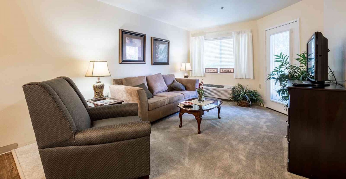 A cozy living room featuring a comfortable sofa, armchair, and coffee table, illuminated by stylish lamps with natural light streaming through a window.
