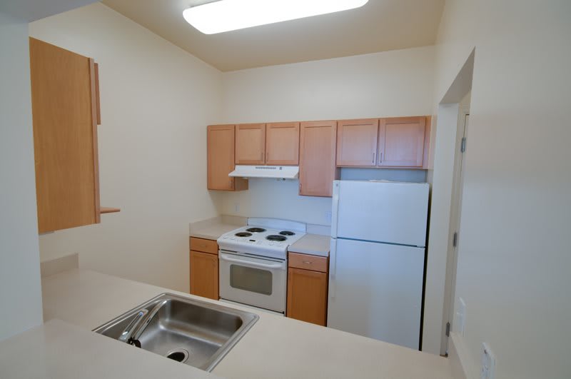 A small apartment kitchen with wooden cabinets, a stove, sink, and refrigerator.