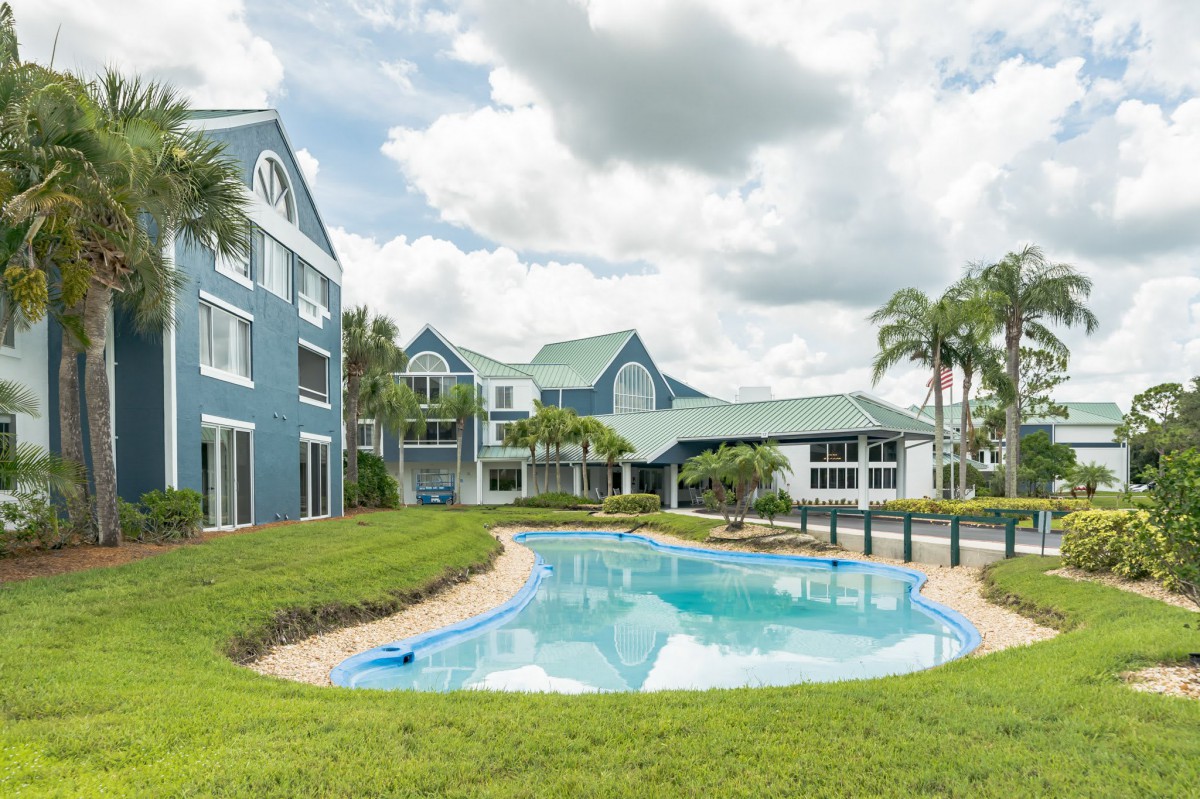 A beautiful residential house with a swimming pool and palm trees under a cloudy sky.