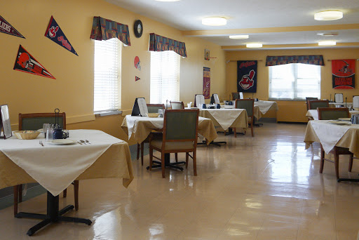An empty dining room with tables and chairs set up, featuring yellow walls and bright lighting.