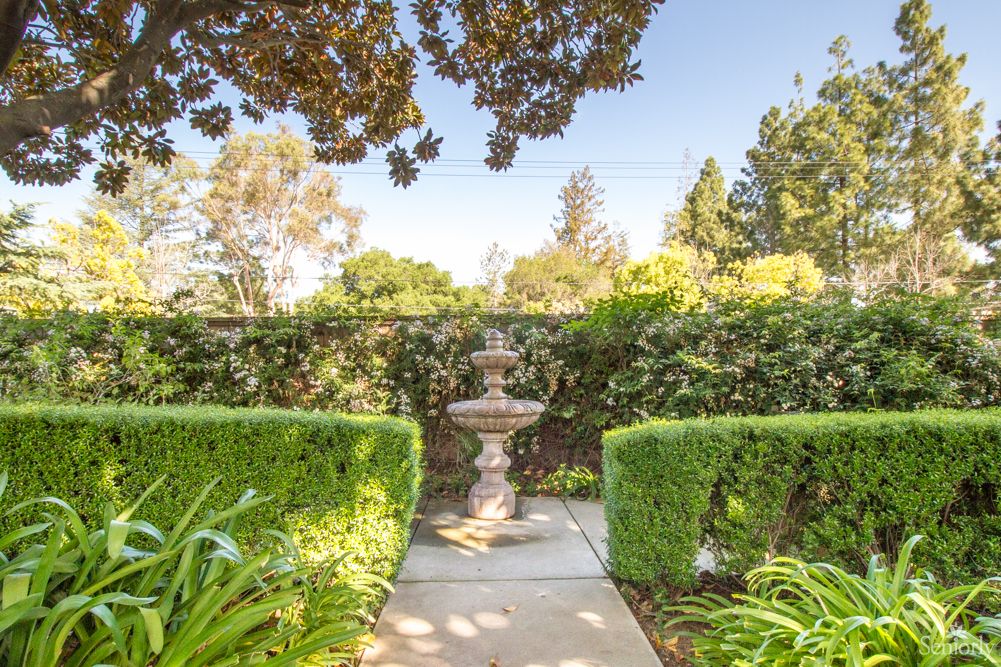 A serene garden pathway with a central fountain surrounded by lush greenery and hedges.