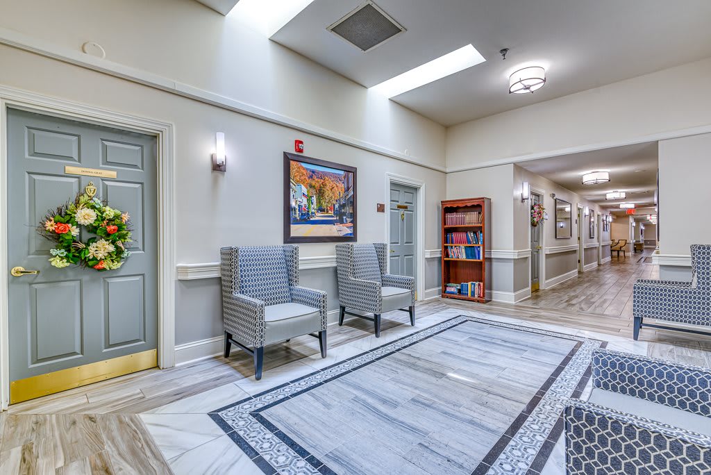 A well-lit hallway with chairs, artwork, and a patterned rug.