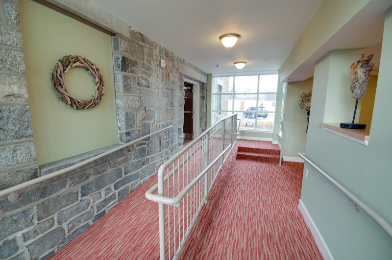 A carpeted hallway with a ramp and handrails, featuring a stone wall and decorative wreath.