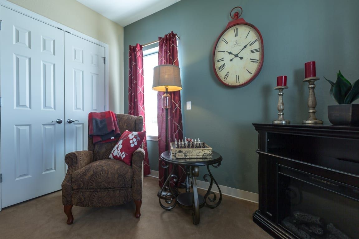 A cozy living room corner with an armchair, chess set, and vintage wall clock.