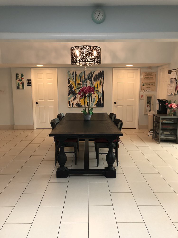 A modern dining room featuring a large wooden table with a decorative vase, surrounded by chairs and illuminated by a chandelier, with artwork adorning the walls.
