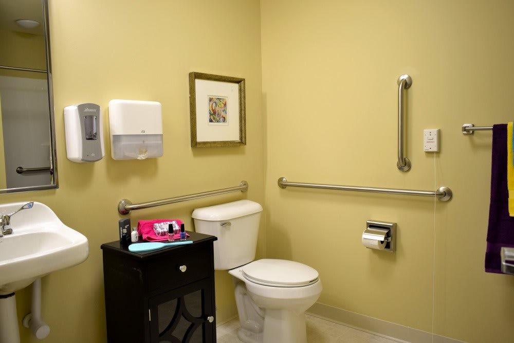 An accessible bathroom with grab bars and a toilet, featuring a sink and paper towel dispenser.