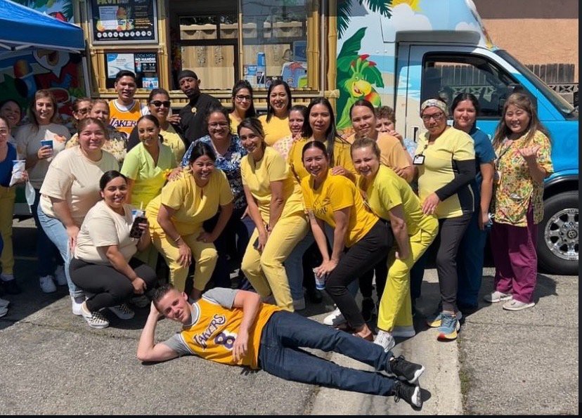 A group of people in yellow shirts pose happily outdoors in front of a colorful vehicle.