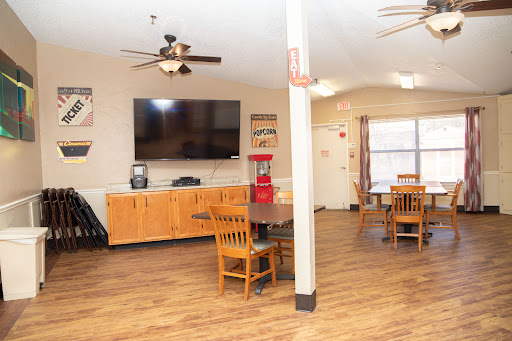 A cozy lounge area featuring wooden furniture, a large television, and ceiling fans.